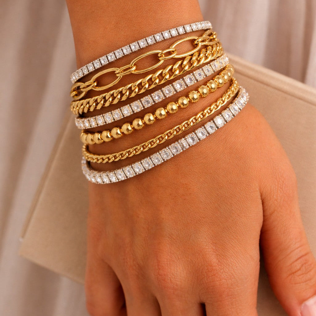 Hand wearing multiple gold and silver bracelets on a neutral background