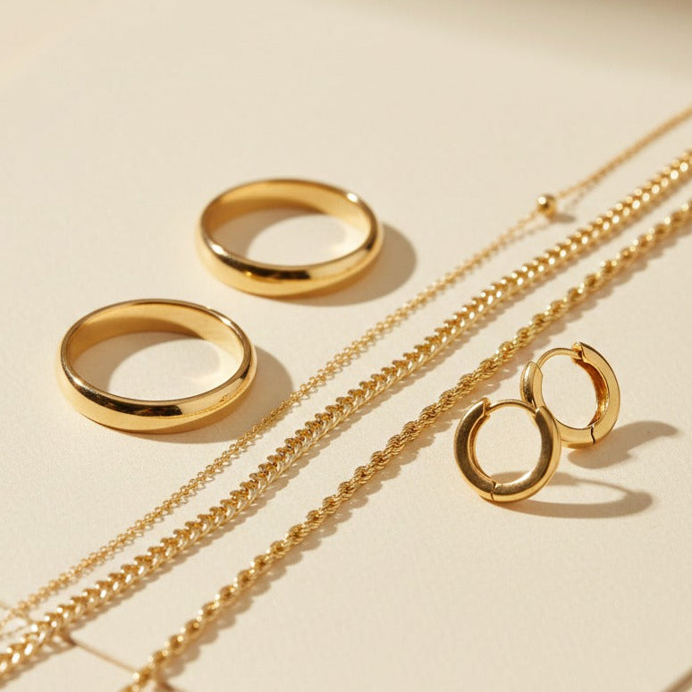 Gold jewelry set including rings and necklaces on a beige surface with 'Prime Jewellery' branding.